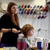 One student in the forefront braiding her hair with another student in the background get her hair adjusted.