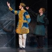 Three male performers in decorative tunics holding their right arms up in exhalation. The middle performer is wearing a crown.