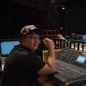 Student sitting inside of McArdle theatre, in front of a soundboard and computer.