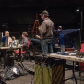 A close-up view of the orchestra pit and the technical crew working with computers. Two students and an instructor are discussing.