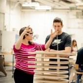 Faculty and a student discussing a wooden stacked project in the forefront.