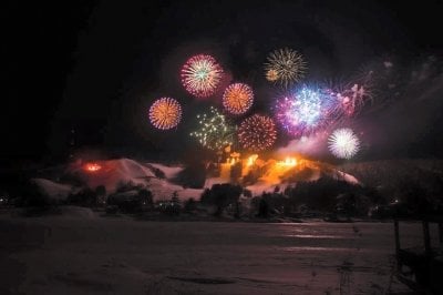 Fireworks are shot in the sky in all colors of the rainbow over a ski hill at night.