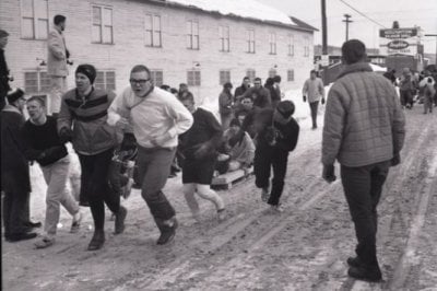 A group of men pull a man in a sled down a street in a black and white photo in winter outside.
